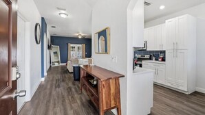 A modern kitchen with white cabinets, a wooden dining table, and a dark blue accent wall. - Welcome to The Chelsea Inn! This cozy, modern 3BR/2BA home is designed for all! (Tampa)