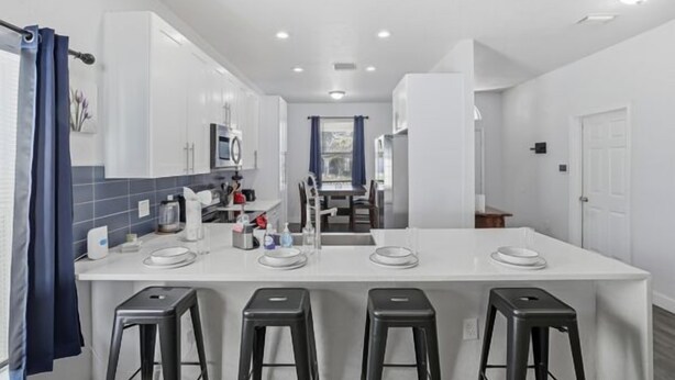 A modern kitchen with a central island, bar stools, and a view into the dining area. - Welcome to The Chelsea Inn! This cozy, modern 3BR/2BA home is designed for all! (Tampa)