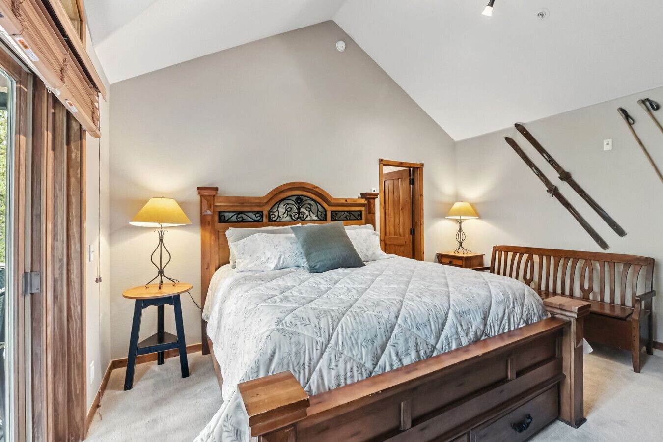A bedroom with a wooden bed, two bedside tables with lamps, a wooden bench, and a sloped ceiling with skylights.