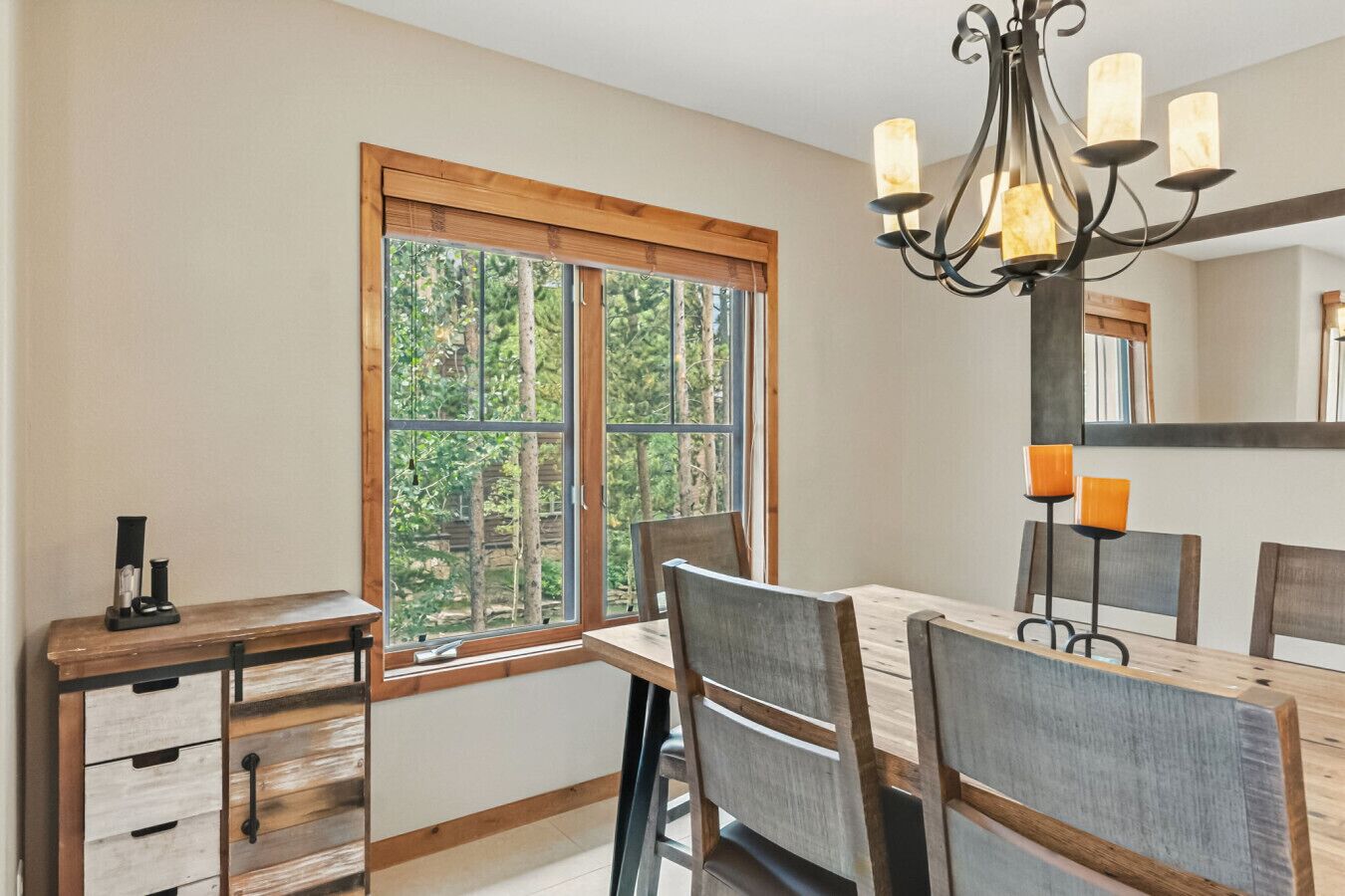 A dining area with a large window, a chandelier, and a wooden table.