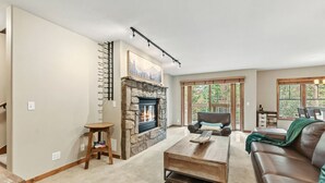 Una sala de estar con chimenea de piedra, un sofá de cuero, una mesa de centro y un comedor con vistas al exterior.