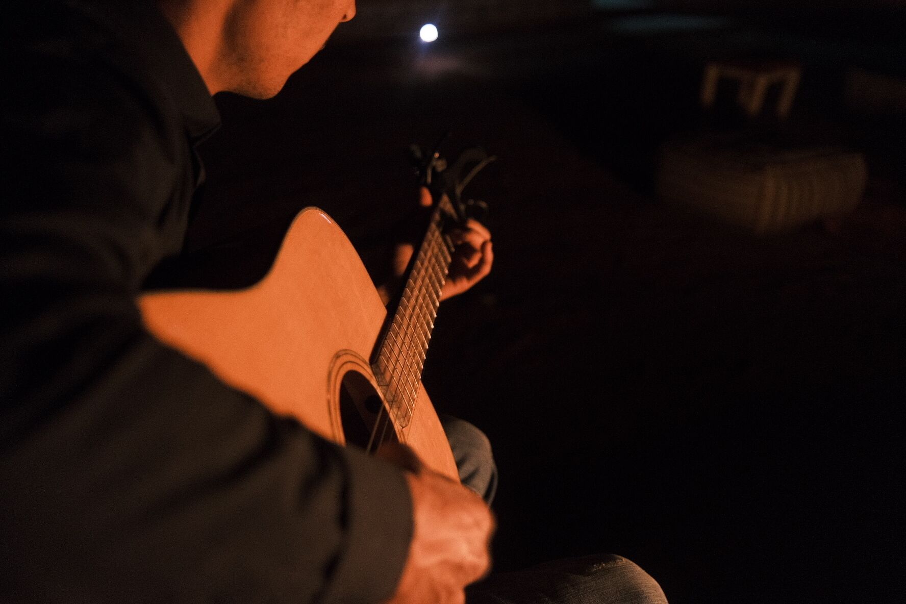 A person playing an acoustic guitar in a dimly lit room.