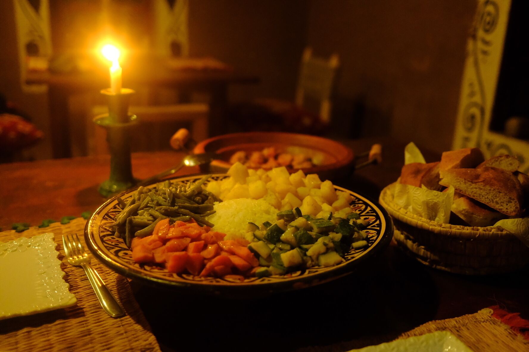 Et spisebord med mad på tallerkenen, et stearinlys og en kurv med brød.