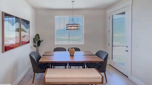 Comedor con mesa de madera, seis sillas, un banco, un florero y una lámpara colgante.