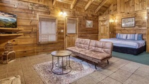 A cozy log cabin room with a bed, a sofa, a small table, and a rug. - Tranquility - Hot-Tub, Fireplace (Pigeon Forge)