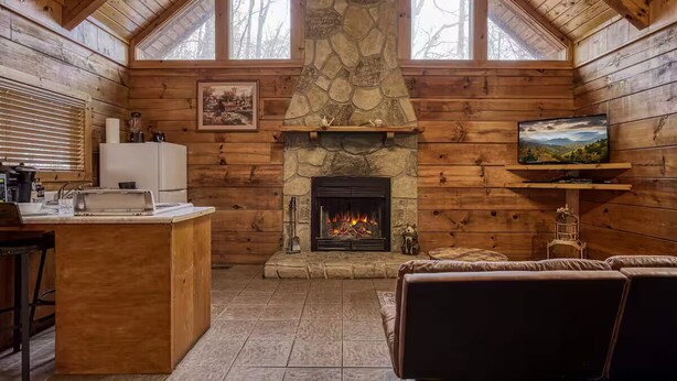 A cozy cabin interior with a stone fireplace, wooden walls, a kitchen area, and a comfortable seating area. - Tranquility - Hot-Tub, Fireplace (Pigeon Forge)