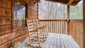 A wooden cabin with a porch featuring rocking chairs and a view of a forest. - Tranquility - Hot-Tub, Fireplace (Pigeon Forge)