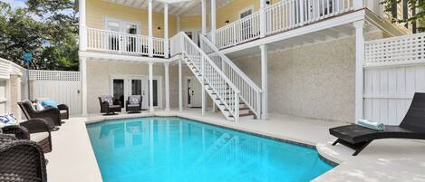 A multi-level outdoor pool area with a staircase, lounge chairs, and a covered seating area.