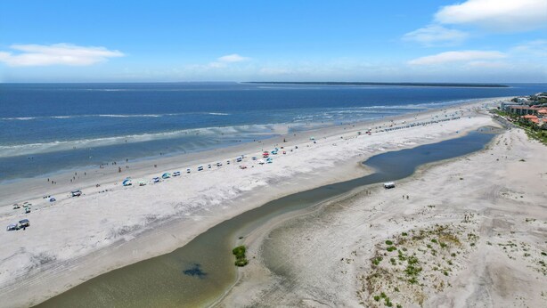 Una playa con una extensa franja de arena, un pequeño canal de agua y una costa distante.