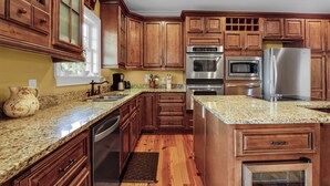 Una cocina con gabinetes de madera, encimeras de granito y electrodomésticos de acero inoxidable, además de un ventanal.