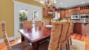 Un comedor con mesa de madera y sillas de mimbre, una araña y armarios de madera al fondo.