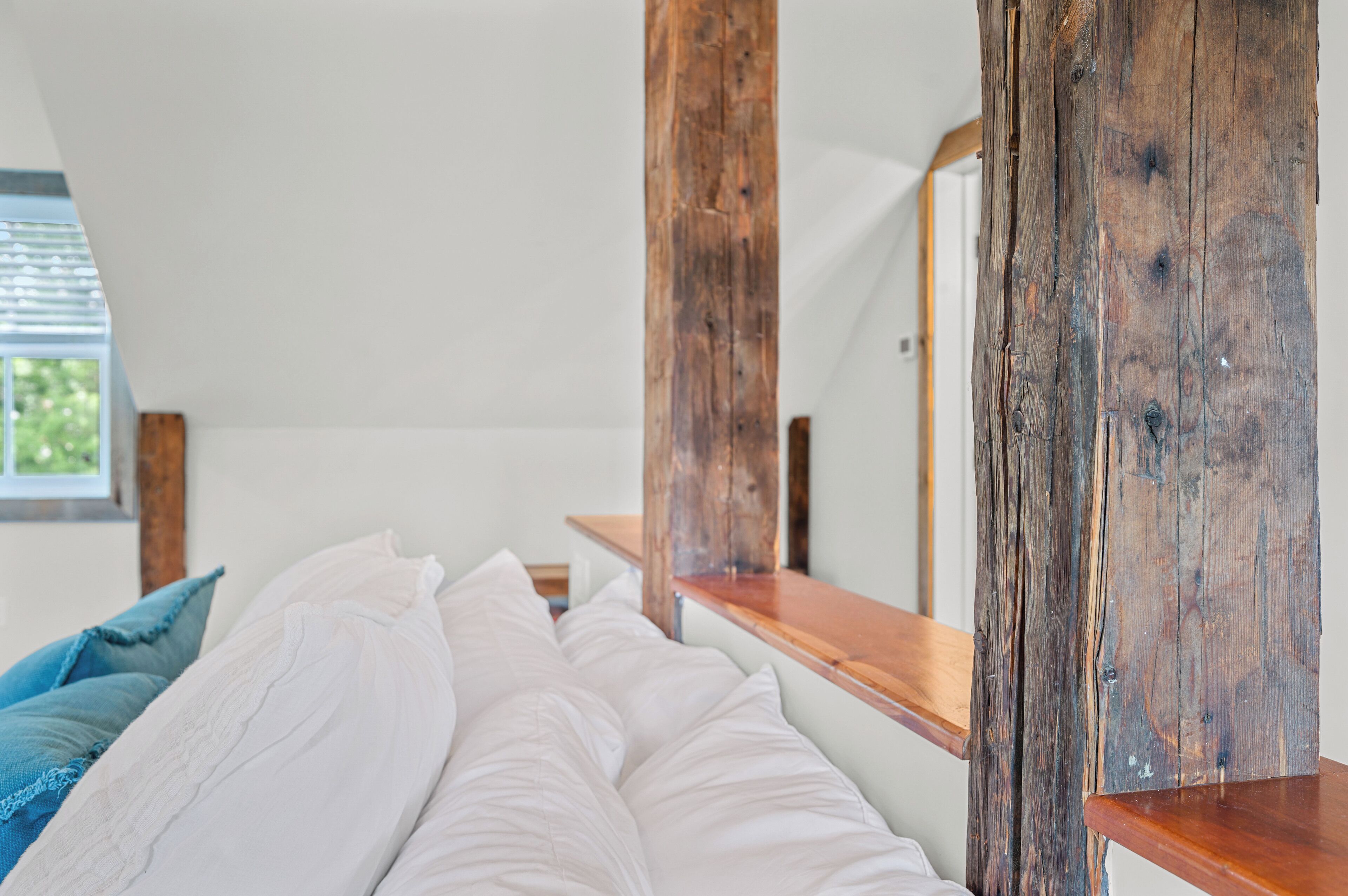 A bedroom with a wooden headboard, a bed with white bedding, and a window with a view of greenery.