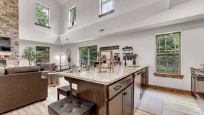 A spacious kitchen with a large island, wooden cabinets, and a stone accent wall. - Creekside Cabin / Branson, SDC, Lakes, In/Out Pool (Hollister)