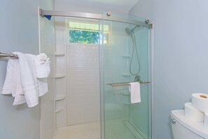 A glass-enclosed shower stall with a window, white tiled walls, and a toilet with toilet paper. - Tilghman Ranch Retreat (North Myrtle Beach)