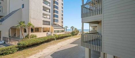 Un edificio de varios pisos con balcones, un sendero pavimentado y vista al mar.