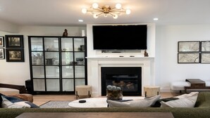 Ein Wohnzimmer mit Kamin, einem Wand-Fernseher und einer Vitrine.