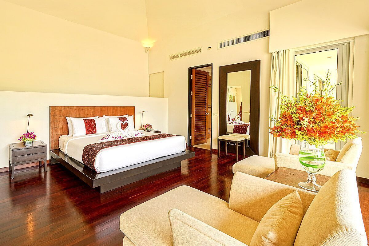 Una habitación de hotel con una cama grande, un sofá, una mesita y un espejo.