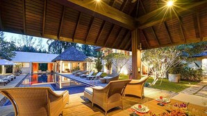 An outdoor pool area with lounge chairs, a dining setup with plates and glasses, and a covered patio with a wooden ceiling. - Villa Samakee (Choeng Thale)