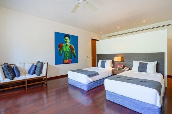 A hotel room with two beds, a sofa, a ceiling fan, and a painting on the wall.