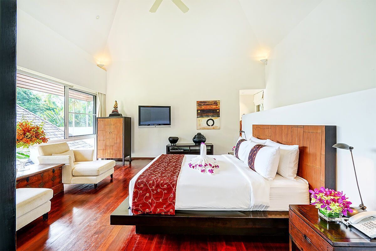 Un dormitorio amplio con una cama grande, cabecera de madera, televisión y vistas al exterior.