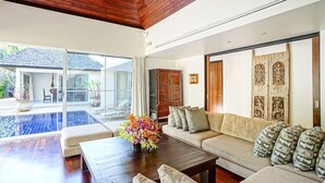 A spacious living area with a wooden ceiling, a large sofa set, a coffee table, and a view of a swimming pool. - Villa Samakee (Choeng Thale)