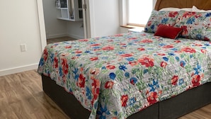 A bedroom with a floral bedspread, a wooden headboard, and a closet with shelves. - Goodturn Cottage (Cody)