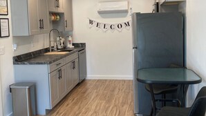 A compact kitchen with grey cabinets, a built-in dishwasher, and a 'WELCOME' banner on the wall. - Goodturn Cottage (Cody)