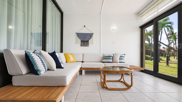 A modern living room with a sofa, coffee table, and large windows offering a view of palm trees.