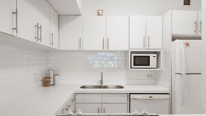 A modern kitchen with white cabinetry, a stainless steel sink, a microwave, and a refrigerator.