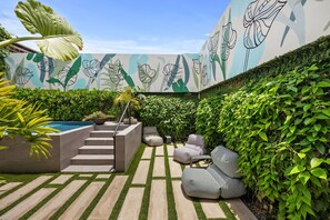 Eine moderne Außenpatio mit Pool, Treppen zu einer Sitzgelegenheit und einem Wandgemälde mit tropischen Blättern.