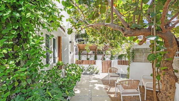 A patio with stone flooring, white chairs, and a tree. - Luxury Condado Apt Walk to the Beach Pool (San Juan)