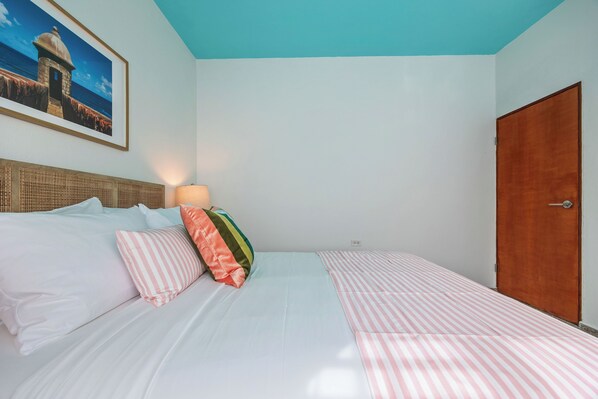 Un dormitorio con cama, almohadas, un cuadro enmarcado en la pared y una puerta de madera.