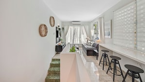 A modern living room with a sofa, a coffee table, and a bar area with stools. There is a staircase leading to another level. - Luxury Condado Apt Walk to the Beach Pool (San Juan)