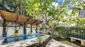 A pool area with a pergola, a small tree, and a bench. - Luxury Condado Apt Walk to the Beach Pool (San Juan)