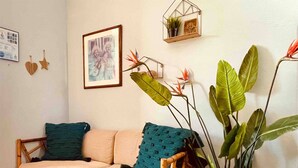 A cozy living room with a sofa, a chair, and a coffee table. There are decorative pillows, a framed picture on the wall, and a small shelf with a plant.
