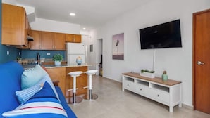 A modern apartment with a kitchen, a living area with a sofa and bar stools, a TV mounted on the wall, and a wooden door. - Coastal Home Safe Secure Parking (San Juan)
