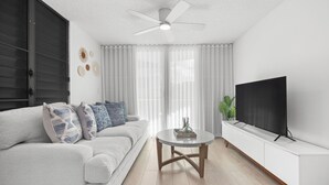 Een moderne woonkamer met een bank, salontafel, televisie en plafondventilator.