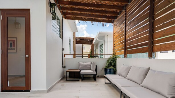 A balcony with a wooden pergola, a sofa, a small table, and a chair. - In Condado Beach Beautiful Pool With Tanning Bed (San Juan)