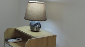 Une table de chevet avec une lampe, une télécommande et un petit tiroir.