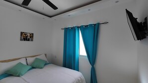 Une chambre à coucher avec un lit, des rideaux de couleur turquoise, un téléviseur fixé au mur et un tableau accroché au mur.