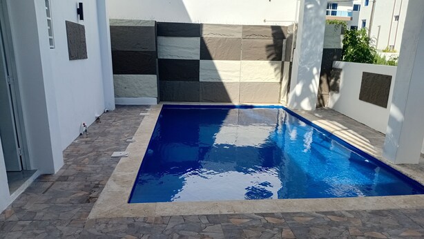 Une piscine dont le sol est recouvert de carreaux de pierre et dont un des murs est blanc, orné d’un motif de carreaux noirs et blancs.