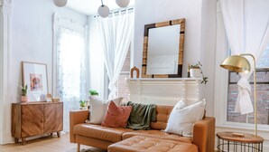 A living room with a brown leather sofa, a wooden cabinet, a round side table, and a large mirror on the wall. - Group-Friendly 4BR / 3.5BA / 2 Kitchens + Private Homes Side-by-Side  Sleeps 10 (Dayton)
