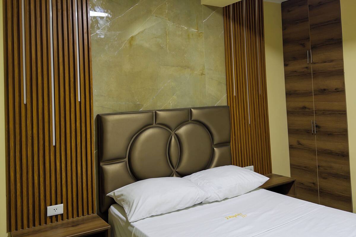 A bedroom with a bed, a nightstand, a wardrobe, and a marble wall.