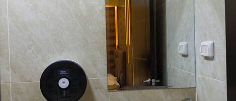 Un baño con inodoro, lavamanos, espejo y dispensador de jabón.