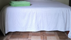 Ein Einzelbett mit weißer Bettdecke und Kissen, ein gerahmtes Bild an der Wand und ein gemusterter Boden.