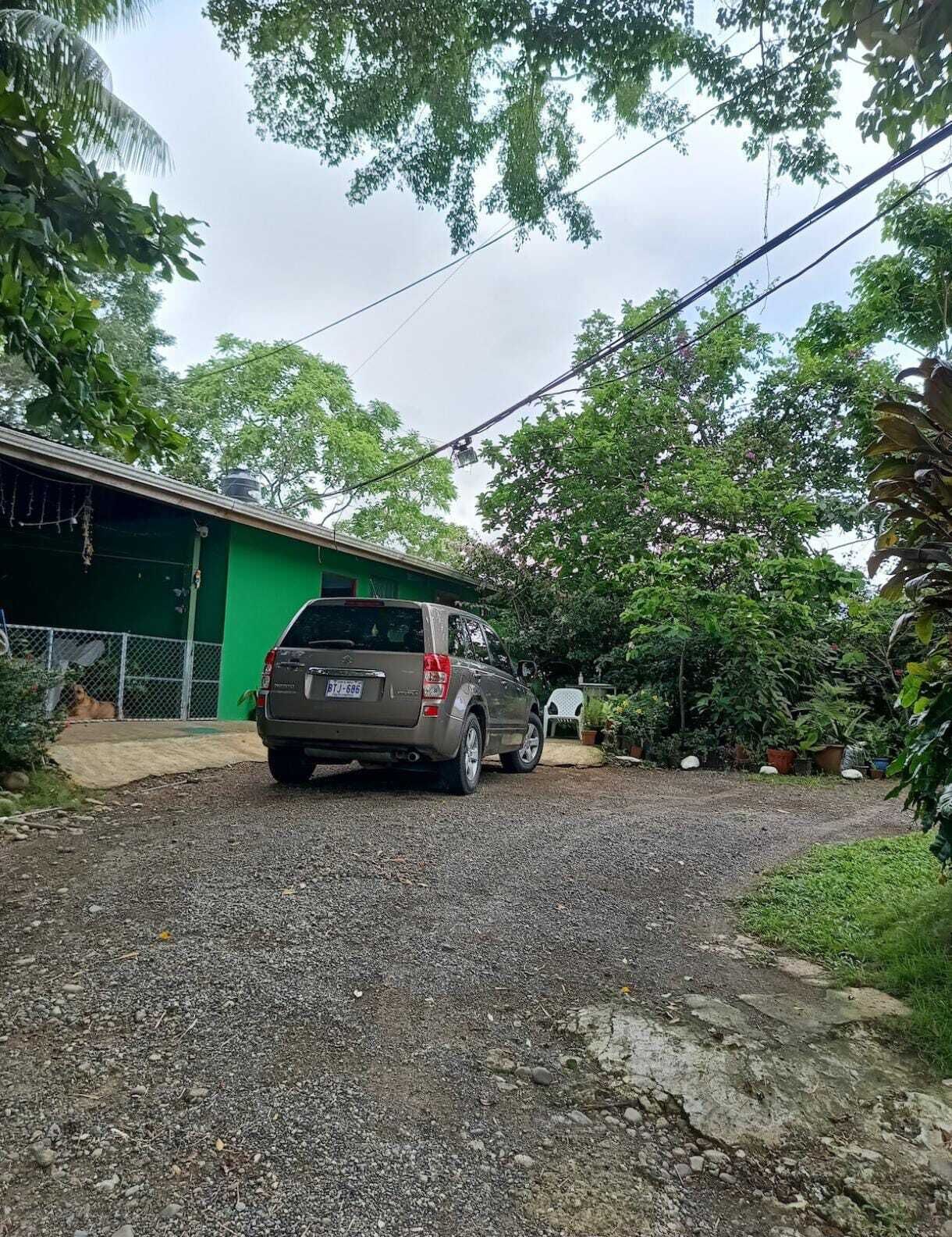 Un camino de grava que conduce a una casa de color verde con un SUV estacionado.
