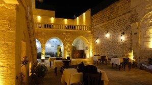 Un espace de restauration en plein air avec des murs et des arches en pierre, des tables recouvertes de nappes jaunes et des plantes en pot.