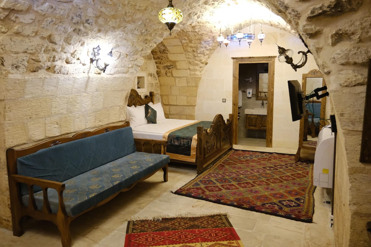 A room with a stone wall, a wooden bed, a blue sofa, and a patterned rug.