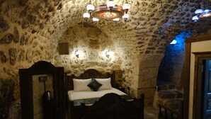 Une chambre aux murs de pierre, avec un lit en bois, un lustre et une petite table.