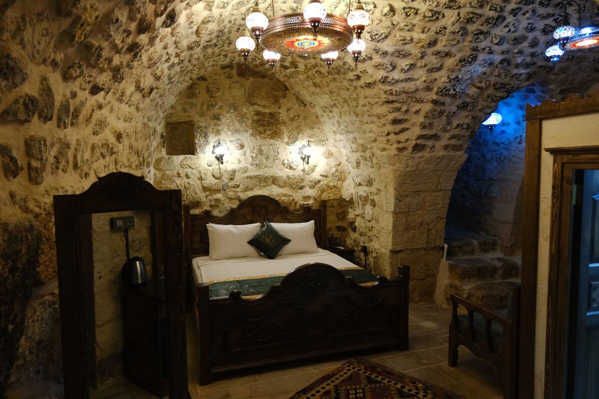 A stone-walled bedroom with a wooden bed, a chandelier, and a small table.